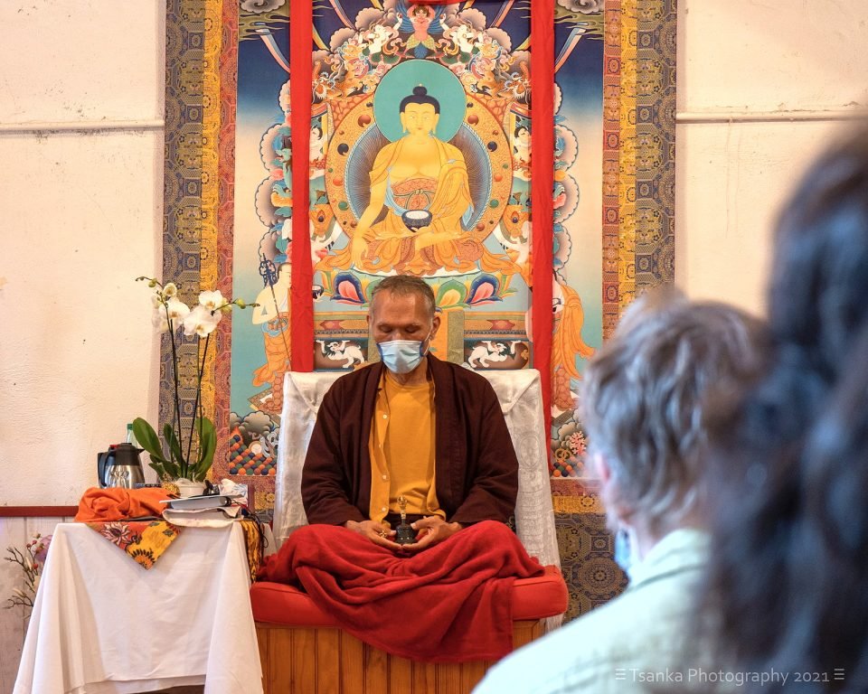 Yangsi Rinpoche sits on an informal throne in front of a large thangka